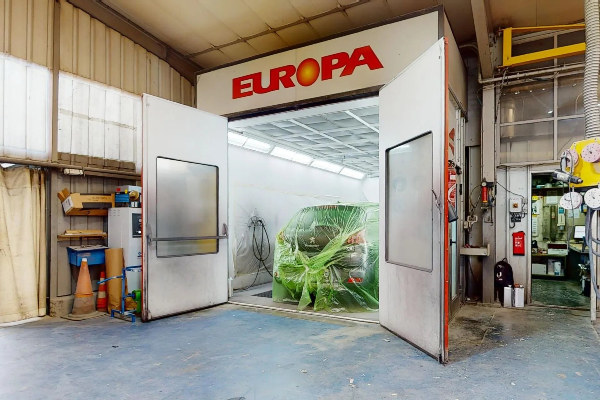 Cabine de peinture Europa de notre atelier de carrosserie, avec une voiture protégée par un film plastique.