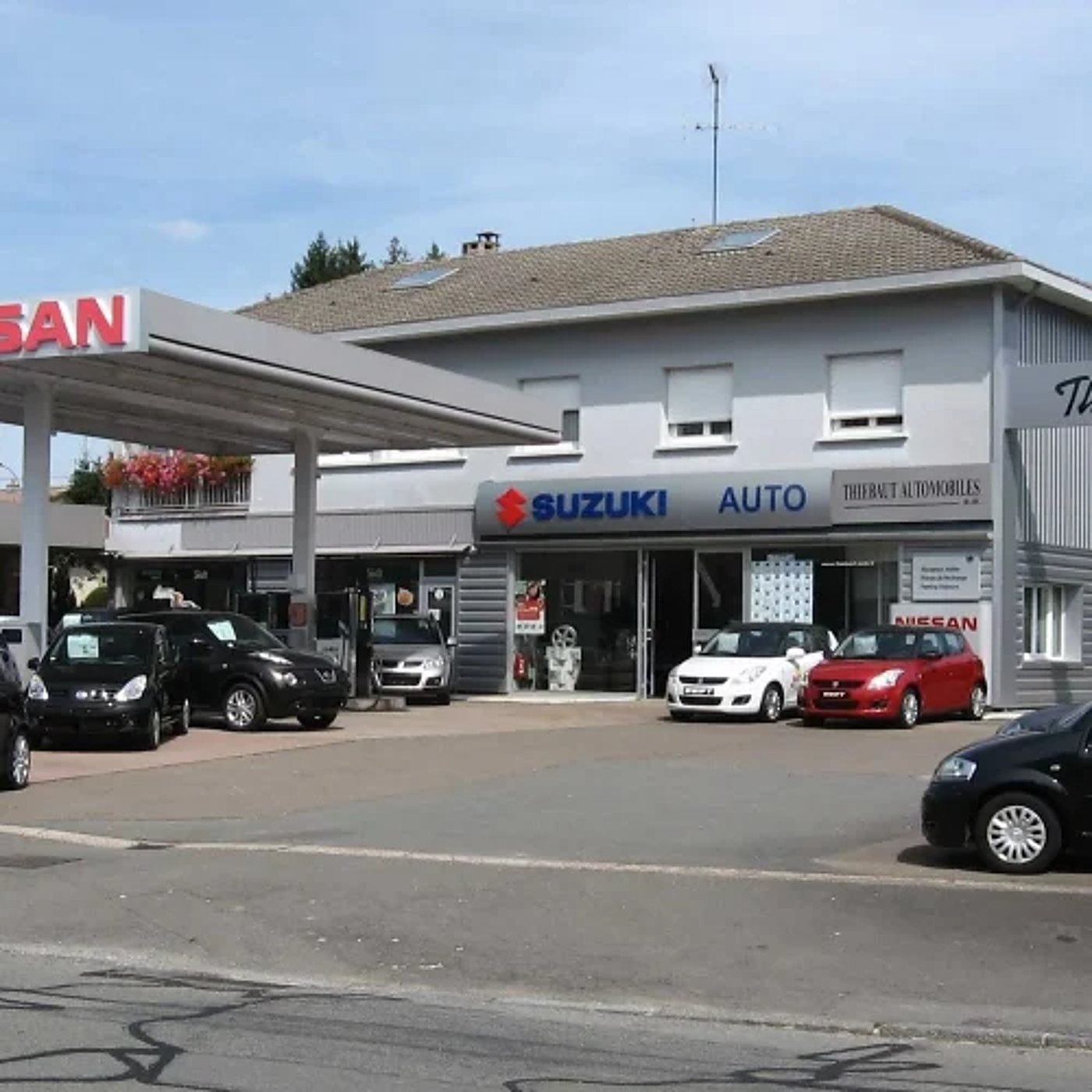 Façade du garage avec des voitures Suzuki garées sur le parking.
