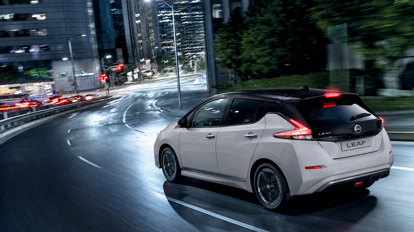Une Nissan Leaf électrique grise à toit noir roulant de nuit en ville.