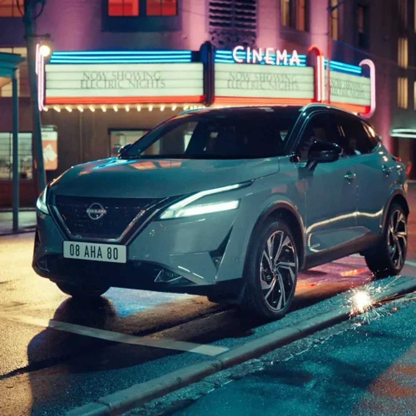 Un SUV Nissan stationné la nuit devant une gare et un cinéma.